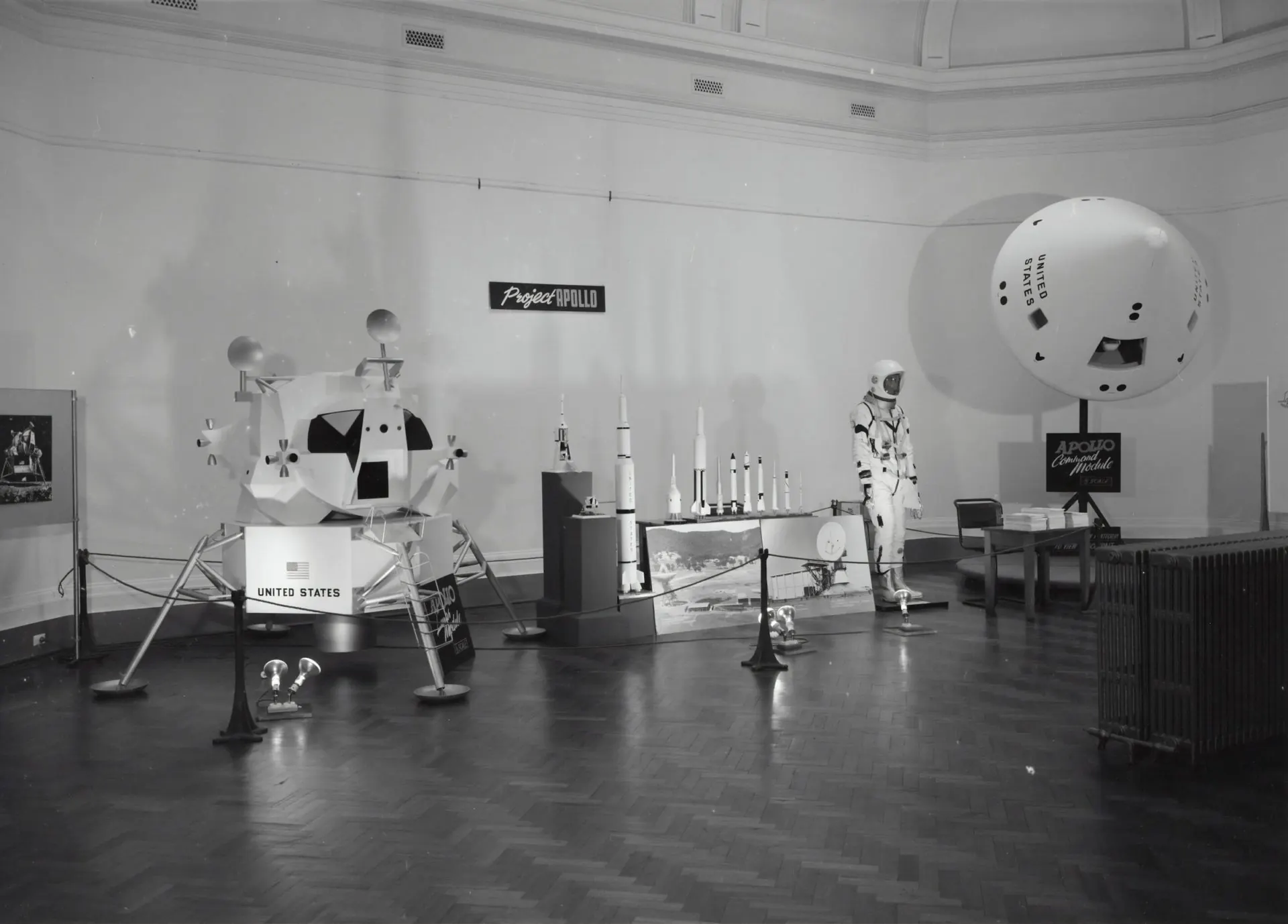 Black-and-white photo of an Apollo exhibition with a lunar module model and a spacesuit